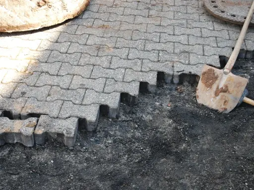Fragment nawierzchni z kostki brukowej w trakcie układania, obok łopata.