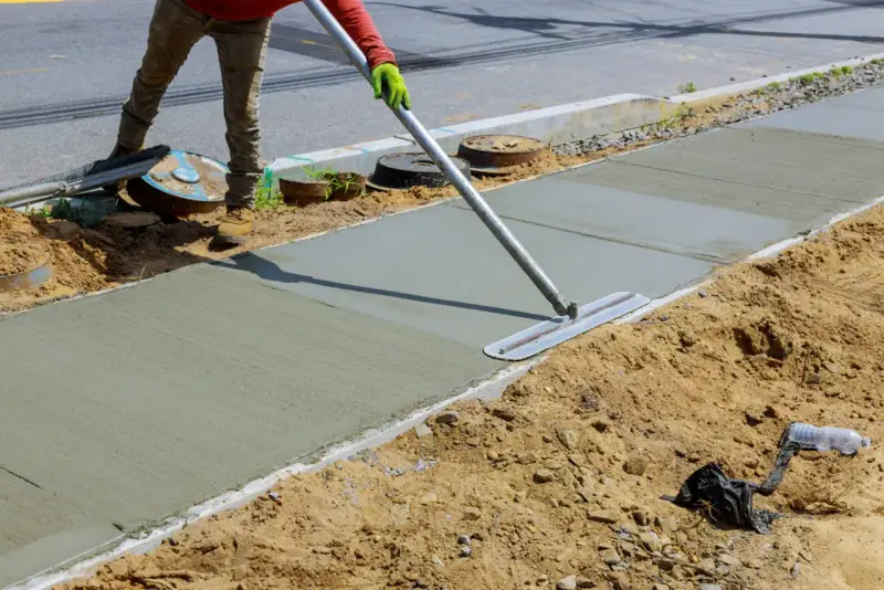 Robotnik wygładza świeży beton na chodniku za pomocą kielni.